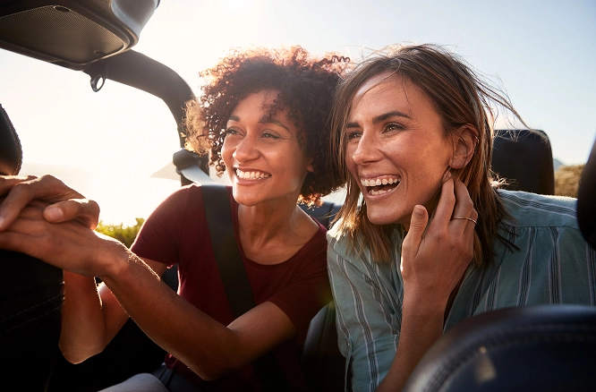 Two healthy women sitting in a parked convertible, enjoying conversation while facing the sunset.