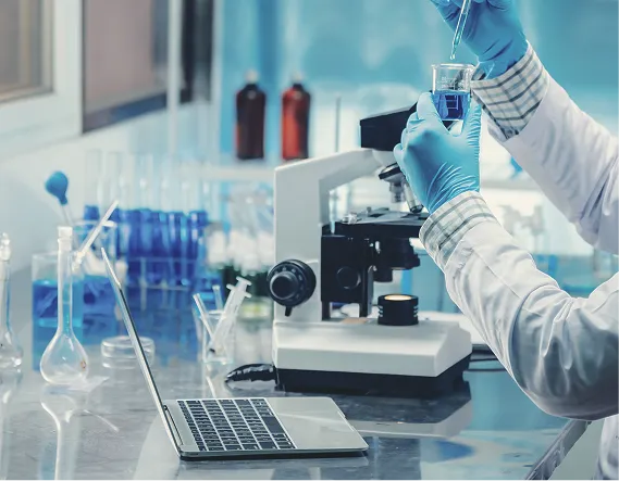 ubiquinol-research-lab-sample-testing Lab technician handling a liquid sample beside a microscope and laptop, representing ingredient testing and research.